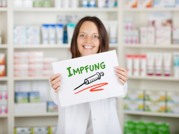 Apothekerin hält Schild mit Aufschrift „Impfung“ hoch
