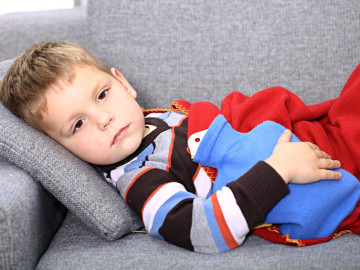 Kleiner Junge mit Wärmflasche auf dem Bauch liegt auf dem Sofa