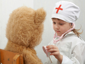 Mädchen als Krankenschwester verkleidet hört ihren Teddybären mit Stethoskop ab