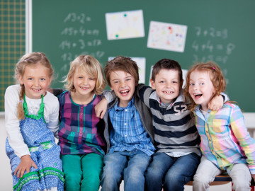 Grundschulkinder sitzen auf einem Tisch vor der Tafel