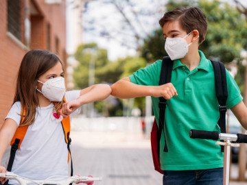 Junge und Mädchen mit FFP2-Maske begrüßen sich mit Ellenbogen-Check