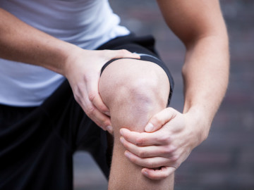 Ein junger Mann in Sportbekleidung fasst sich an sein Knie. 