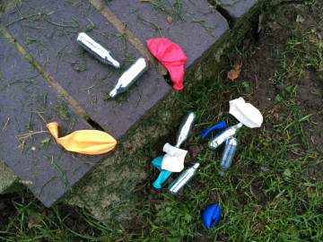 Lachgaskartuschen und Luftballons liegen auf dem Boden