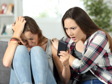Trauiges Mädchen zeigt ihrer Freundin ein Smartphone mit schlechten Neuigkeiten