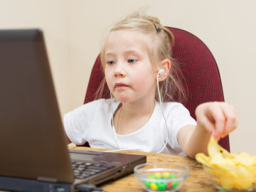 Mädchen vor dem Laptop greift mit der Hand zu Chips