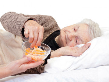 Bettlägerige Seniorin nimmt sich ein Stück Mandarine aus einem gereichten Schälchen