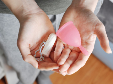 Frau hält verschiedene Hygieneprodukte (Tampon, Menstruationstasse) in der Hand