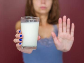 Frau hält Glas Milch gestreckt nach vorne und symbolisiert mit dem anderen Arm „Stopp“

