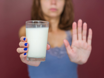 Frau hält Glas Milch gestreckt nach vorne und symbolisiert mit dem anderen Arm „Stopp“

