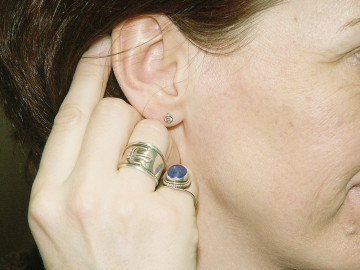 Frau hält Hand mit Ringen ans Ohr mit Ohrring