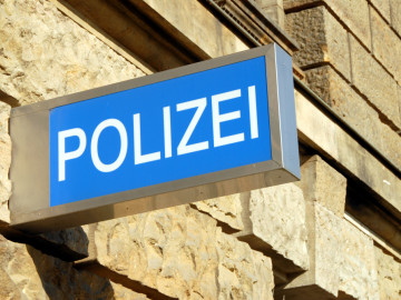 Eine Sandsteinmauer, an der ein blaues Polizeischild hängt.