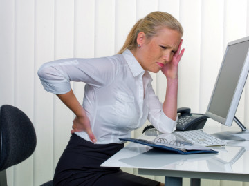 Frau mit Rückenschmerzen sitzt vor dem Computer
