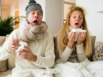 Erkältetes Pärchen sitzt auf der Couch und niest