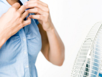 Frau knöpft sich vor einem Ventilator die Bluse auf
