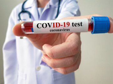Arzt hält Teströhrchen mit Aufschrift COVID-19 Test in die Kamera