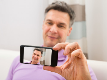 Mann mit Handy, auf dem ein Selfie zu sehen ist