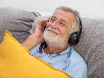 Älterer Mann hört mit Kopfhörern auf dem Sofa Musik