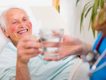 Seniorin erhält von einer Pflegekraft ein Glas Wasser
