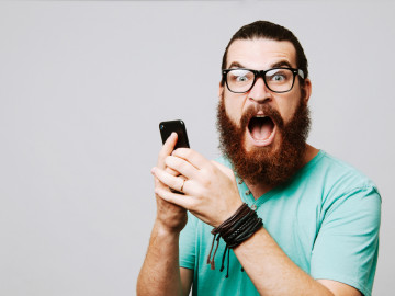 Junger Mann mit Brille schreit und hält ein Smartphone in der Hand
