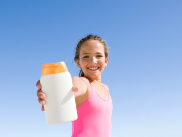 Mädchen im Badeanzug hält Sonnencremeflasche in die Kamera