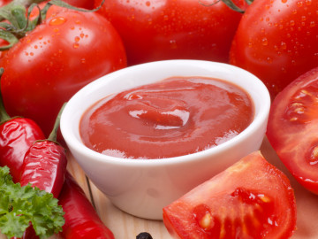 rohe, rote Tomaten und Chilischoten, gruppiert um eine kleine Schale Ketchup.