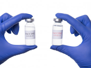 Blaubehandschuhte Hände halten zwei Vials mit Impfstoff