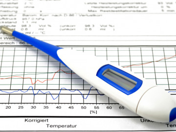 Fieberthermometer, welches auf einem Blatt mit einer Temperaturkurve liegt.