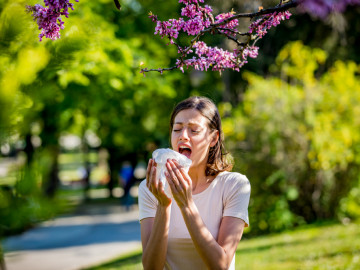 Frau niest in ein Taschentuch unter blühendem Zweig