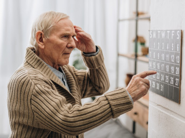 Alter Mann schaut und zeigt auf einen Kalender und fast sich an den Kopf