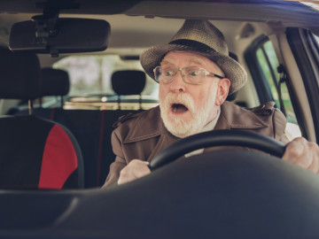 Senior mit Hut mit überraschtem Gesicht am Steuer eines Autos