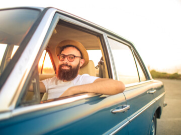 Mann mit Vollbart und Sonnenhut im Auto mit heruntergekurbeltem Fenster