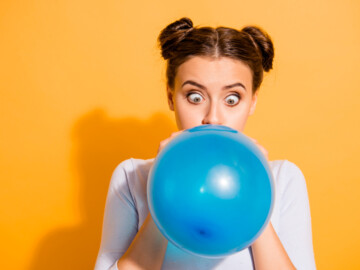 Schielende junge Frau pustet einen blauen Luftballon auf