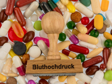 Stempel mit Aufschrift „Bluthochdruck“ auf verschiedenen bunten Tabletten und Kapseln