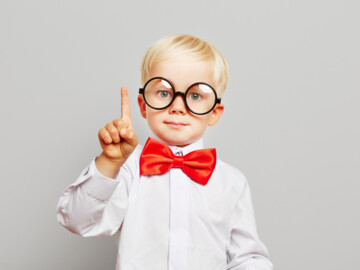 Kind mit großer schwarzer Brille mit runden Gläsern hebt den Zeigefinger