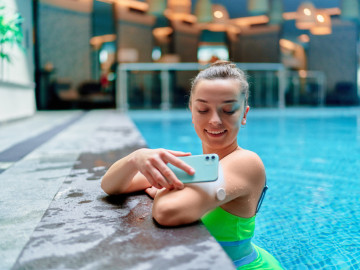 Diabetikerin im Swimming-Pool mit Mess-Systeme zur kontinuierlichen Glukosemessung (CGM) ruft Daten per Smartphone ab