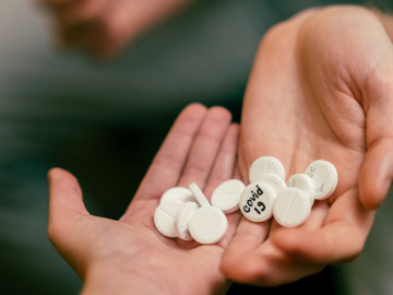 Tabletten mit Aufschrift COVID-19 in zwei Händen gehalten