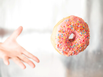 Hand wirft einen pinkfarbenen Donut mit bunten Streuseln