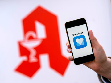Rotes Apotheken-A im Hintergrund, im Vordergrund Handy mit Anzeige „E-Rezept“