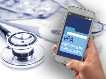 Hand hält Handy mit Ansicht  ePA-Ordner und Schrift „elektronische Patientenakte, daneben liegt ein Stethoskop, im Hintergrund Fieberthermometer und Tablettenblister (verschwommen)