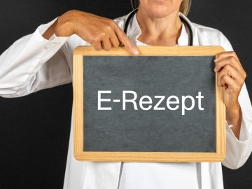 Frau im weißen Kittel hält Kreidetafel mit Aufschrift E-Rezept in den Händen