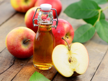 Apfelessig in Bügelflasche auf Holztisch umgeben von Äpfeln