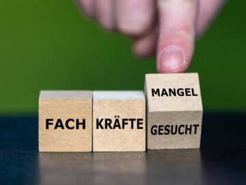 Hand dreht Würfel und ändert den Ausdruck „Fachkräfte gesucht“ in „Fachkräftemangel“.