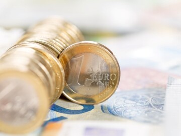 Eine Reihe von Euromünzen auf einem 20-Euro-Schein. Ein Münze schert aus der Reihe aus