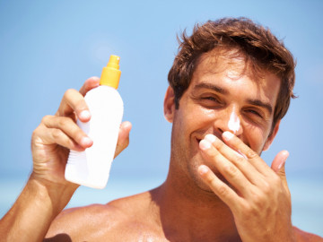 Mann unter freiem Himmel, mit einem Kosmetikprodukt in der Hand und Creme auf der Nase.