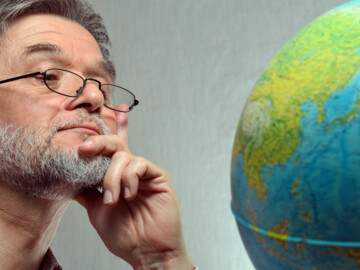 Mann mit Lesebrille schaut Globus an