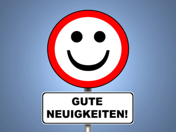 Rundes Schild mit rotem Rand und lachendem Smilie, darunter ein weiteres Schild mit der Aufschrift „Gute Neuigkeiten“
