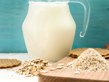 Krug mit Hafermilch, davor kernige und feine Haferflocken und Haferkeks