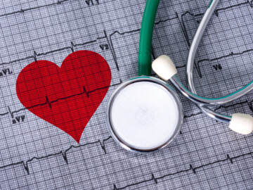 Rotes Herz auf einem EKG-Ausdruck, daneben ein Stethoskop eines Blutdruckmessgerätes