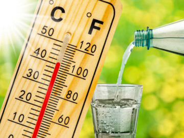 Holzthermometer zeigt über 40 Grad Celsius an, daneben ein Glas, in das aus einer Flasche Wasser eingegossen wird.
