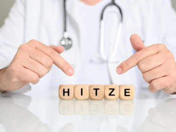Mann mit Stethoskop um den Hals zeigt auf Holzwürfel, die das Wort HITZE bilden